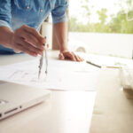 Ein Mann misst mit einem Zirkel auf einem Bauplan