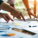 Menschen diskutieren über Unterlagen die auf einem Schreibtisch liegen